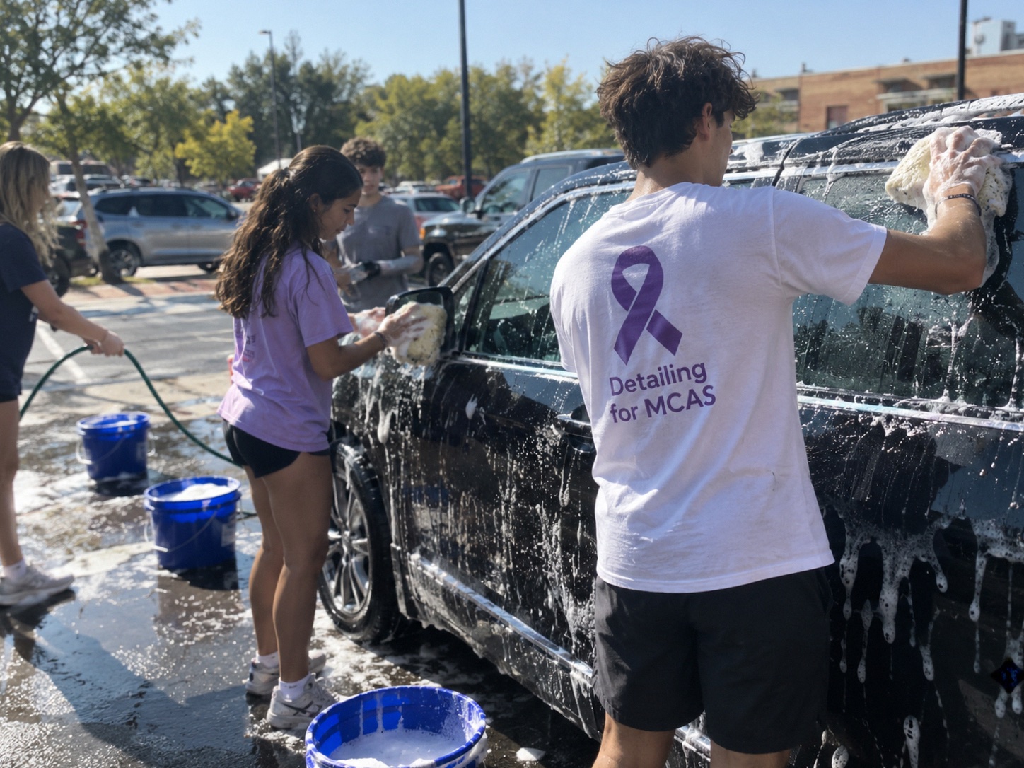 Detailing for MCAS volunteers washing a car at a fundraiser, one in a branded purple-ribbon shirt